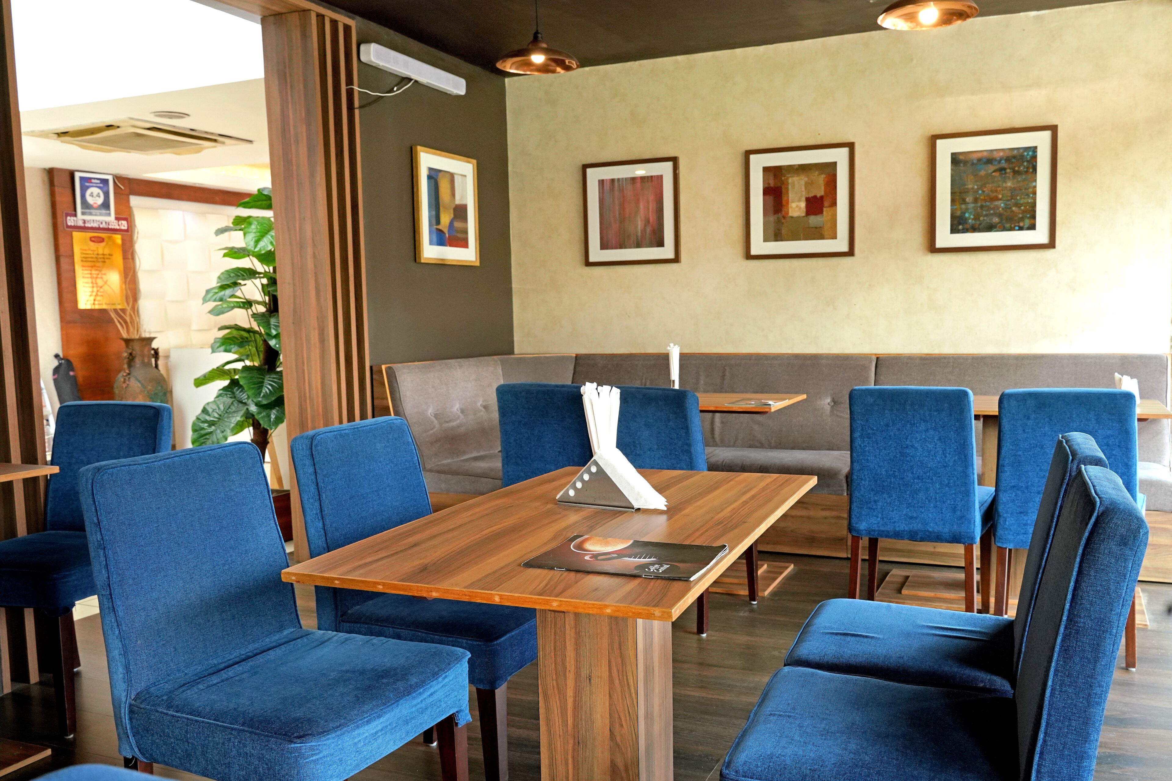 A restaurant with blue upholstered chairs, a wooden table, and a grey booth.