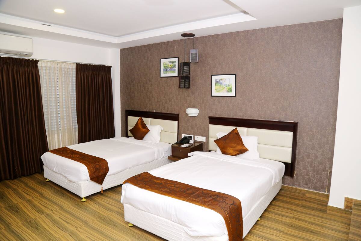 Een hotelkamer met twee bedden, een nachtkastje en een wandairconditioning.