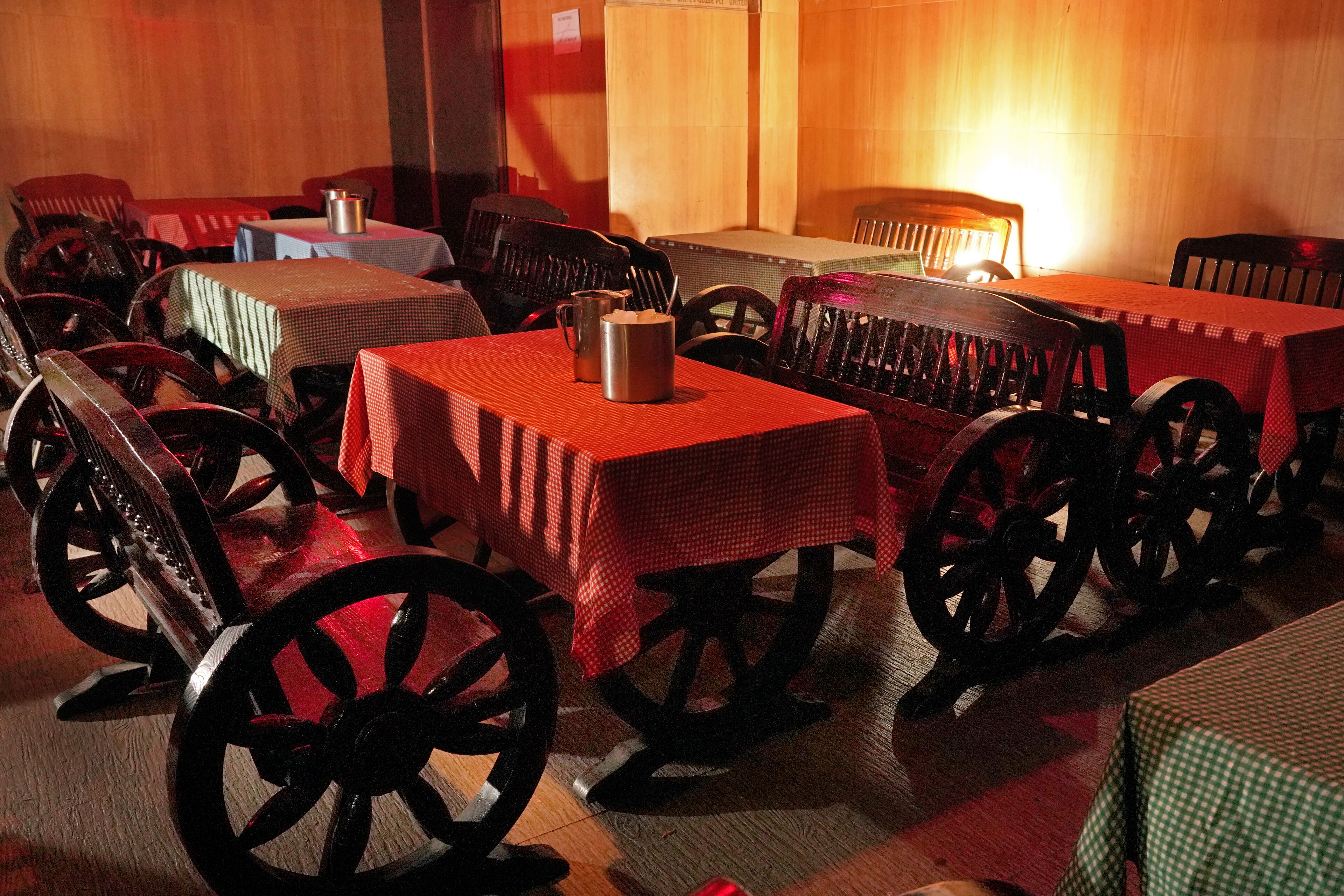 Un restaurant avec de nombreuses tables recouvertes de nappes à carreaux rouges et verts, des chaises en bois et de vieux rouets d’époque.