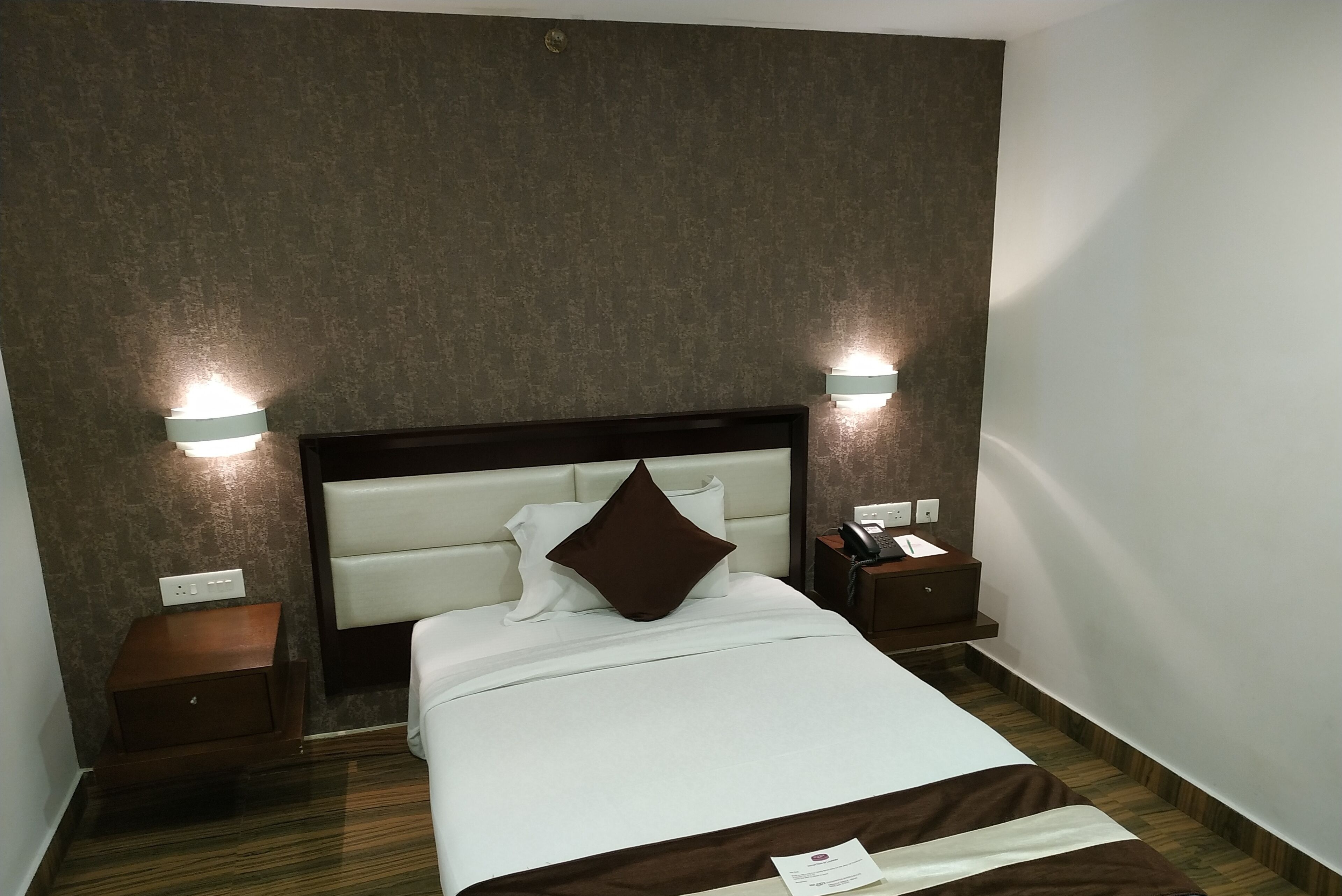 Habitación de hotel con cama, dos mesitas de noche y un teléfono de pared.