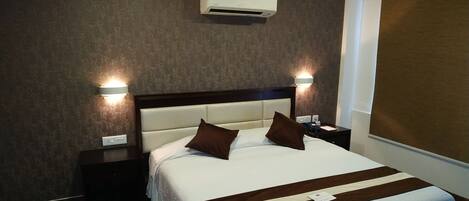 A hotel room with a large bed, two bedside tables, an air conditioning unit, and a wall-mounted light fixture.