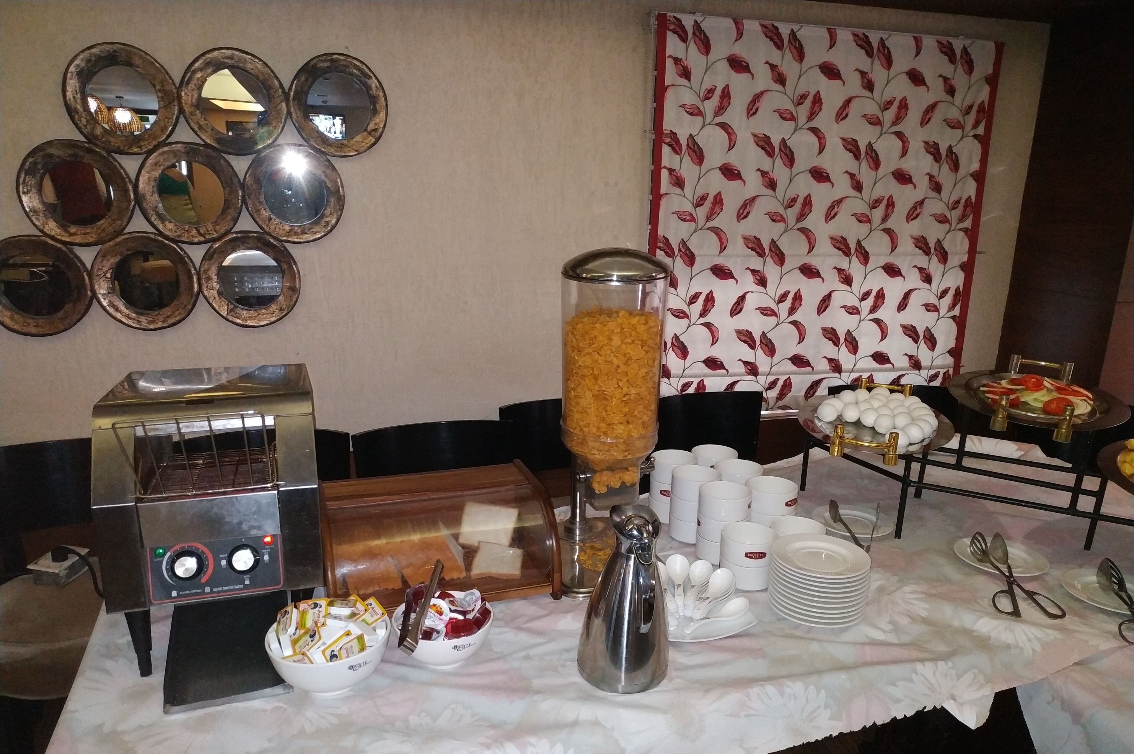 A breakfast buffet setup with a coffee machine, cereal dispenser, and various breakfast items.