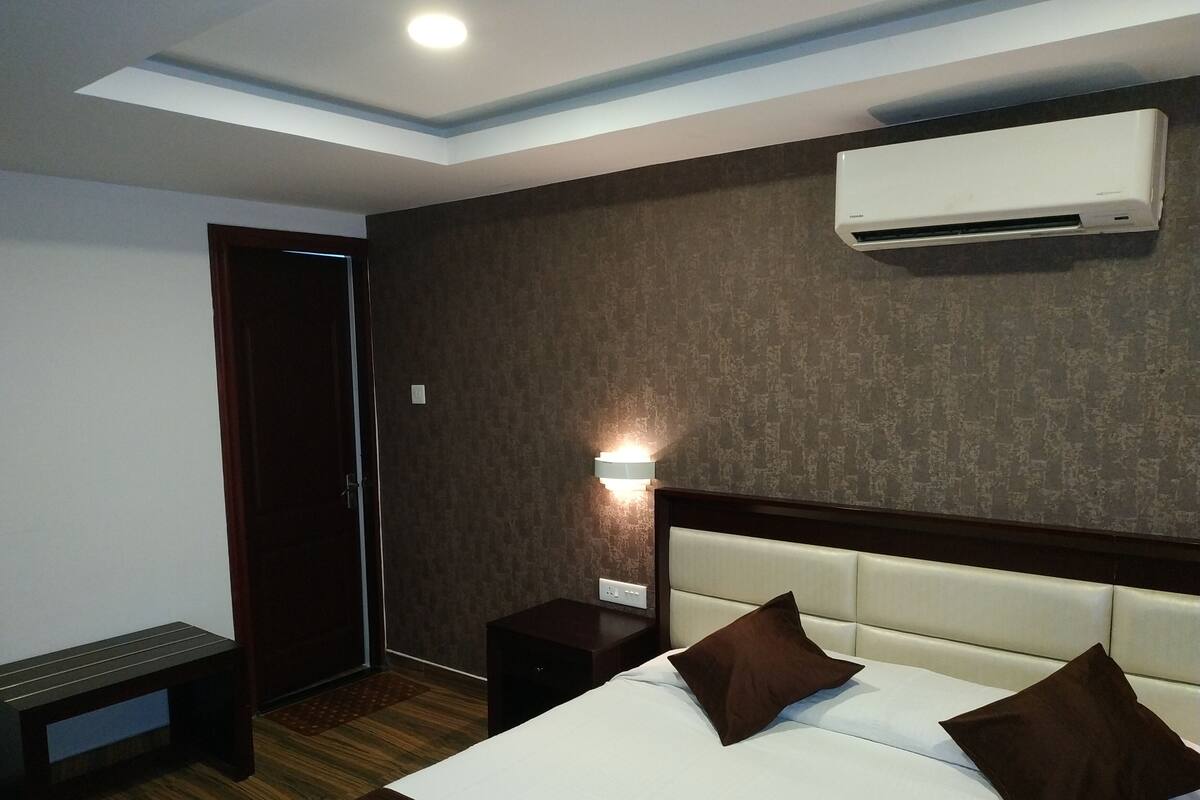 Hotelkamer met een bed, nachtkastjes, een airconditioning en een lampje aan de muur, en een deur.