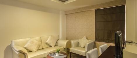 Een moderne woonkamer met een bank, fauteuils, een salontafel en een flatscreen televisie.