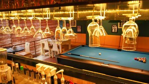 Zona de bar con mesa de billar, taburetes y una variedad de botellas y vasos.