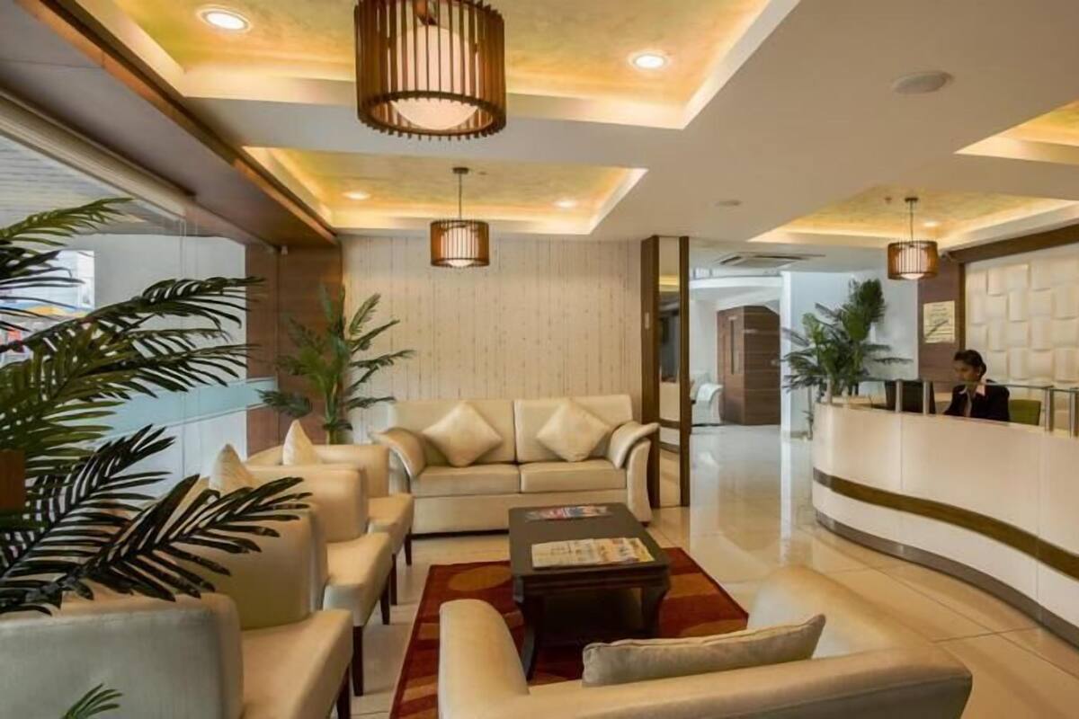 Een hotel lobby met een receptiebalie, zithoek met sofa's en fauteuils, en een grote potplant.