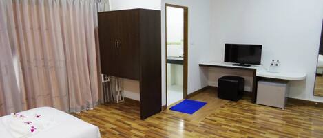 A hotel room with a bed, a desk with a television, a small kitchenette, and a bathroom visible through a door.