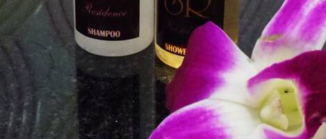 Dos botellas de champú y gel de ducha SR sobre una superficie reflectante con una orquídea morada.