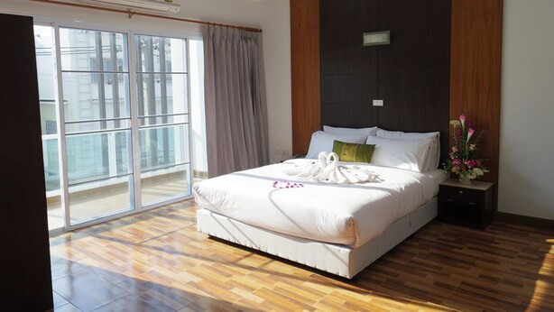 A hotel room with a large bed, a wooden floor, a sliding glass door to the balcony, and a nightstand with a vase of flowers. - THE SR Residence Lampang (Lampang)