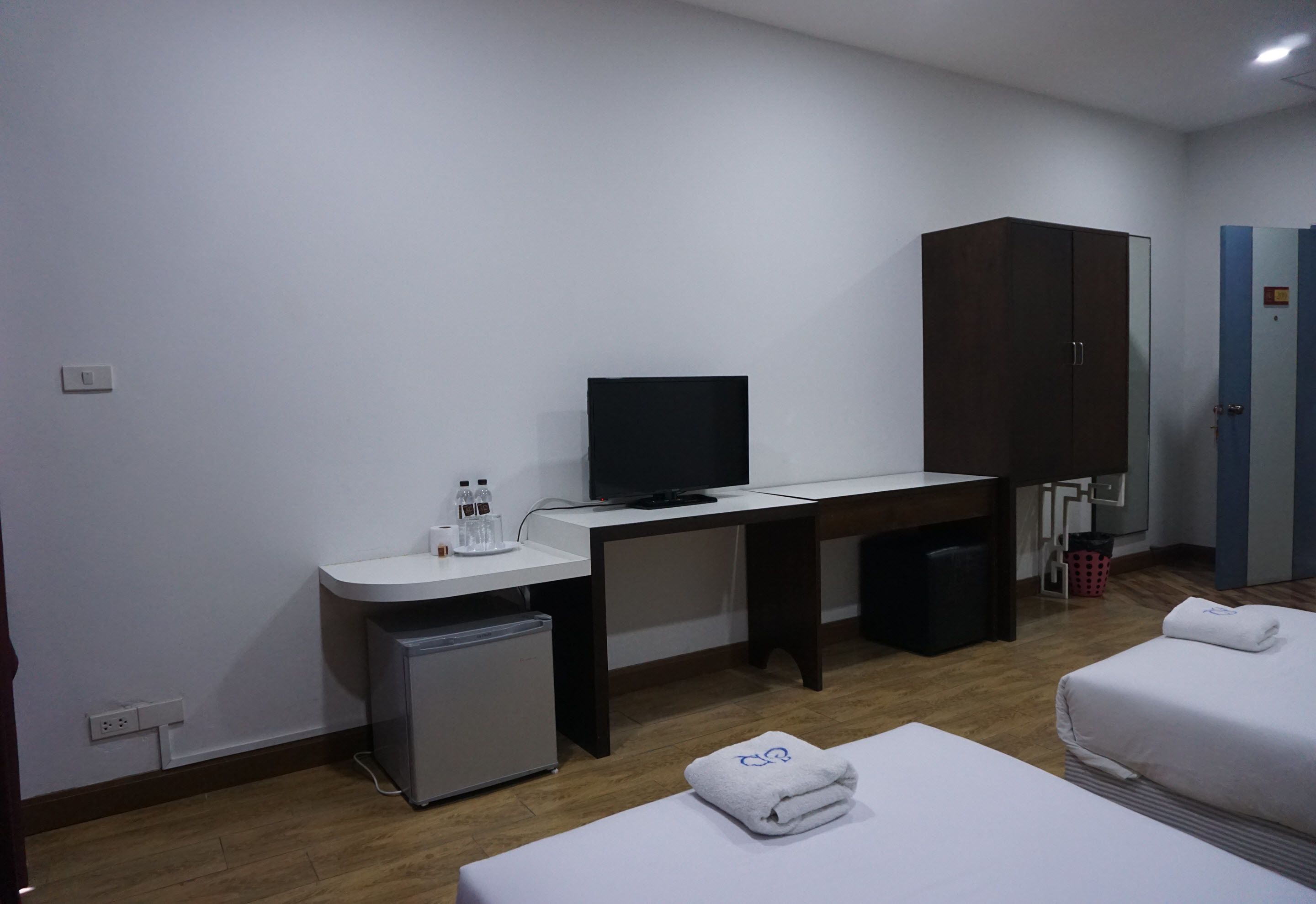 A hotel room with a bed, a desk with a television, a small fridge, a wardrobe, and a bathroom.