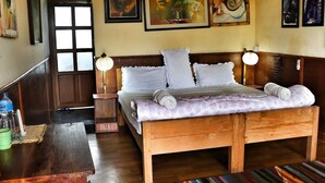 A wooden bed with white linens and pillows, a bedside table with a lamp, and a door with a window. - Lake Twenty Thousand Farm and Retreat (Bharatpur)