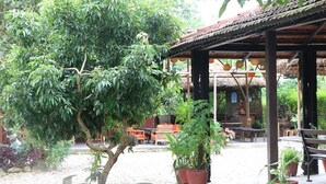 A covered outdoor seating area with tables and chairs, surrounded by potted plants and a tree. - Lake Twenty Thousand Farm and Retreat (Bharatpur)