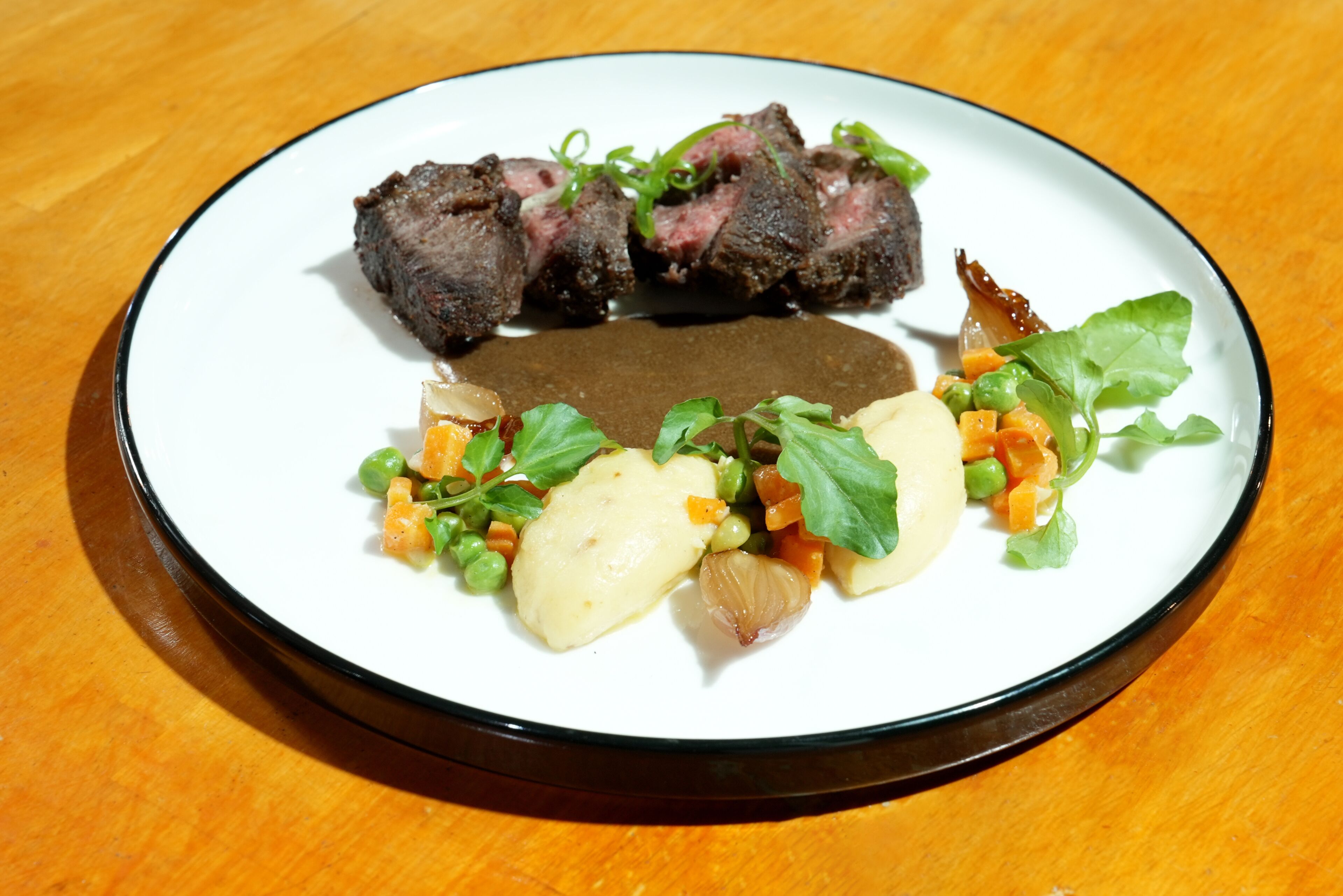 Un plato con bistec, puré de papas, guisantes, zanahorias y verduras de hoja.