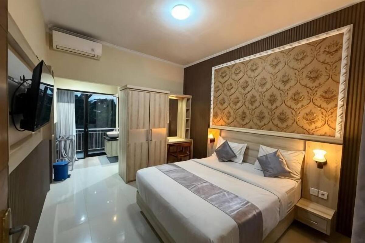 A hotel room with a large bed, a TV mounted on the wall, a balcony with a view, and a decorative headboard.