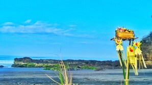Eine Strandansicht mit blauem Himmel, felsiger Küste und einem Zierbauwerk mit Korb auf dem Dach.