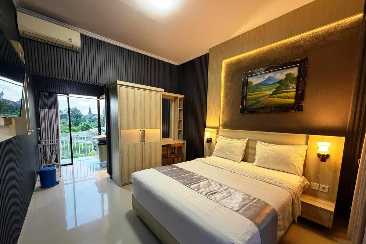 A modern hotel room with a large bed, a desk, a wardrobe, and a balcony with a view.