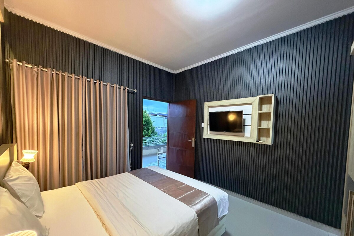 A hotel room with a bed, a TV mounted on the wall, and a door leading to an outdoor area.
