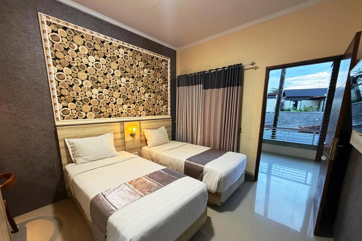 A hotel room with two beds, a decorative wall, a view through a glass door, and a wooden floor.