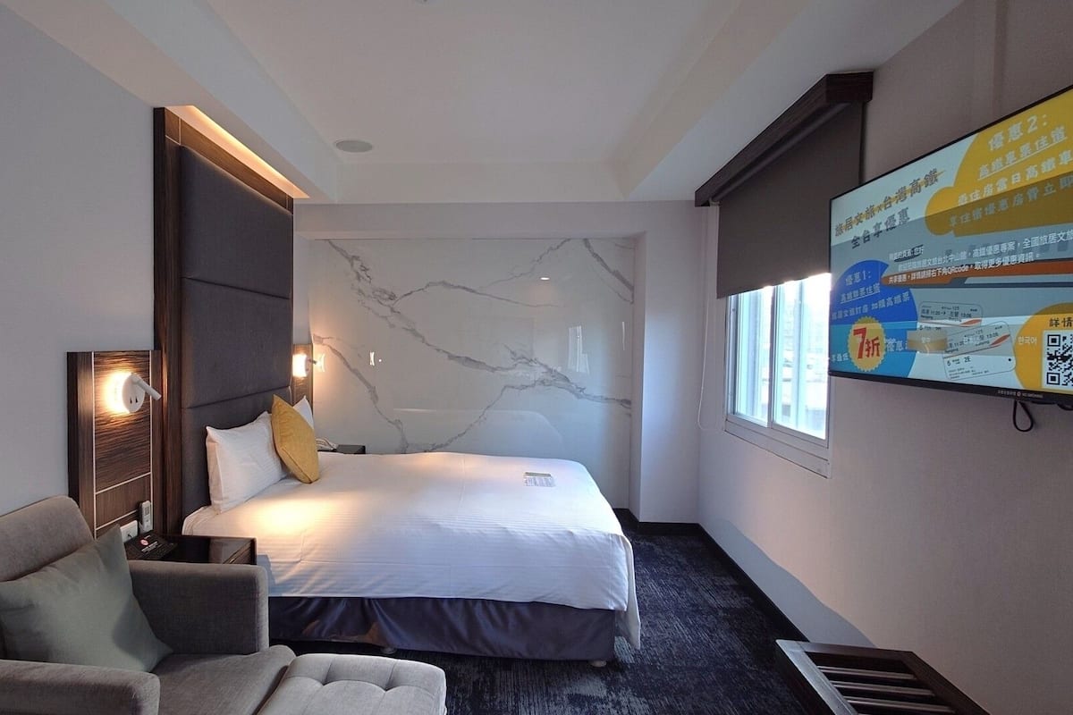 A hotel room with a bed, a desk, a chair, a TV, and a marble-patterned wall.