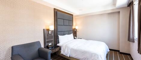 A hotel room with a bed, a chair, a nightstand, and a wall-mounted lamp.