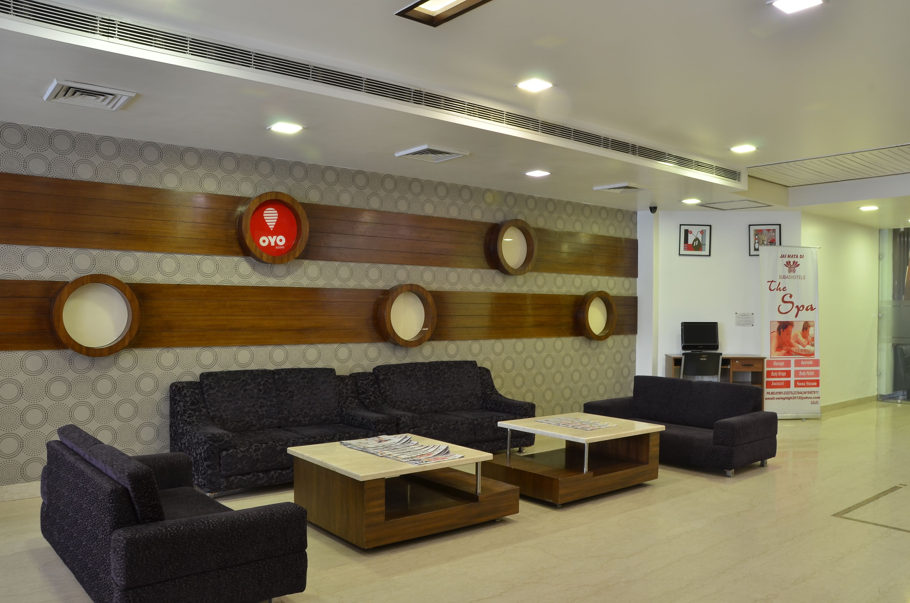 A hotel reception area with a modern design, featuring a reception desk, sofas, and a wall with circular mirrors and a wooden panel design.