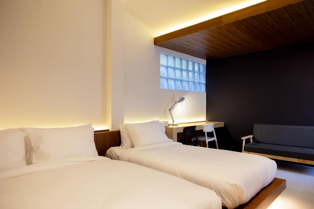 A modern hotel room with two beds, a desk, a chair, and a sofa.