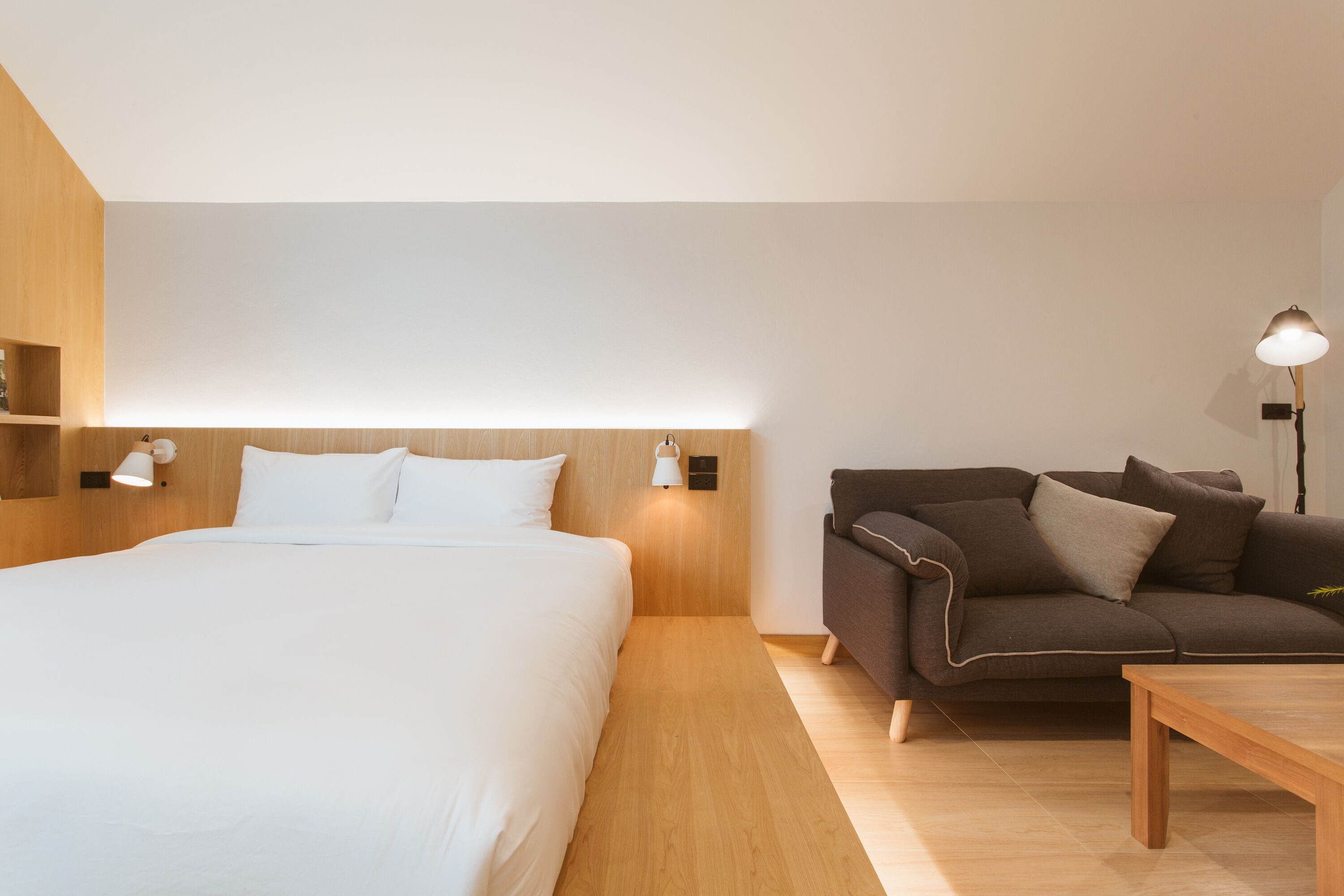 Una habitación de hotel moderna con una cama grande, una mesita de noche de madera, un sofá marrón y una pequeña mesa.