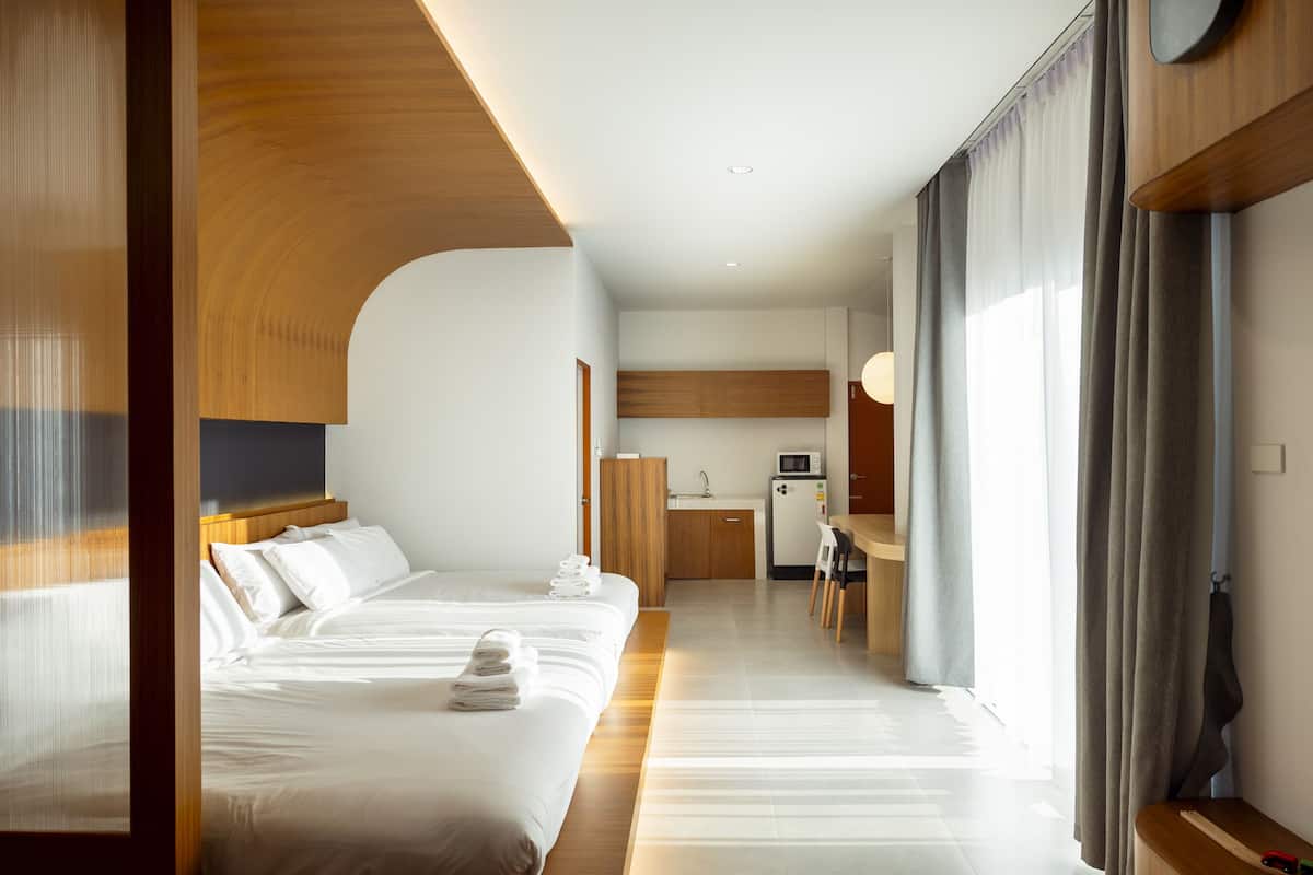 A hotel room with two beds, a kitchenette, and a large window with curtains.