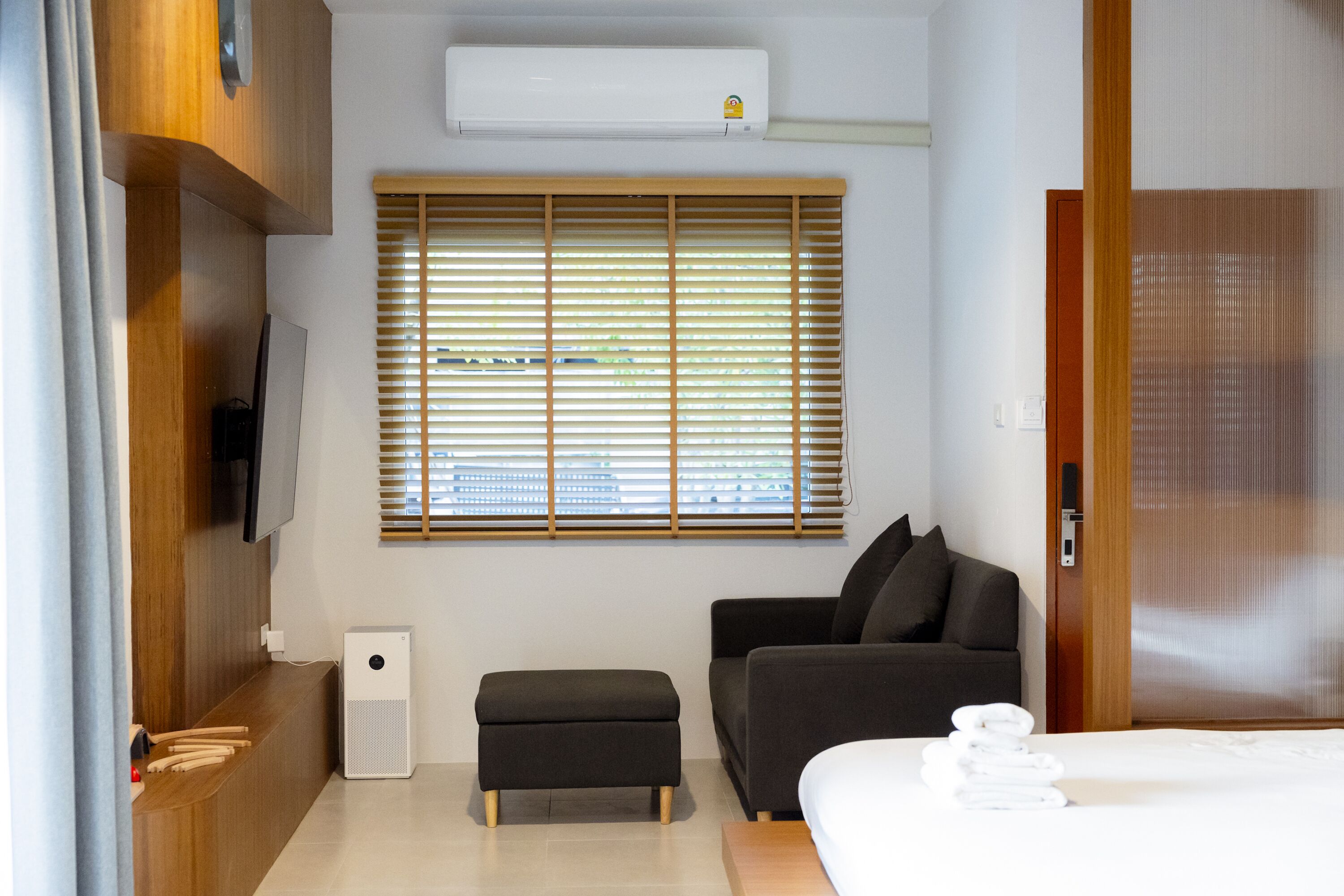 Una habitación de hotel moderna con una cama, un sofá, una mesita, un televisor y un ventanal con persianas.