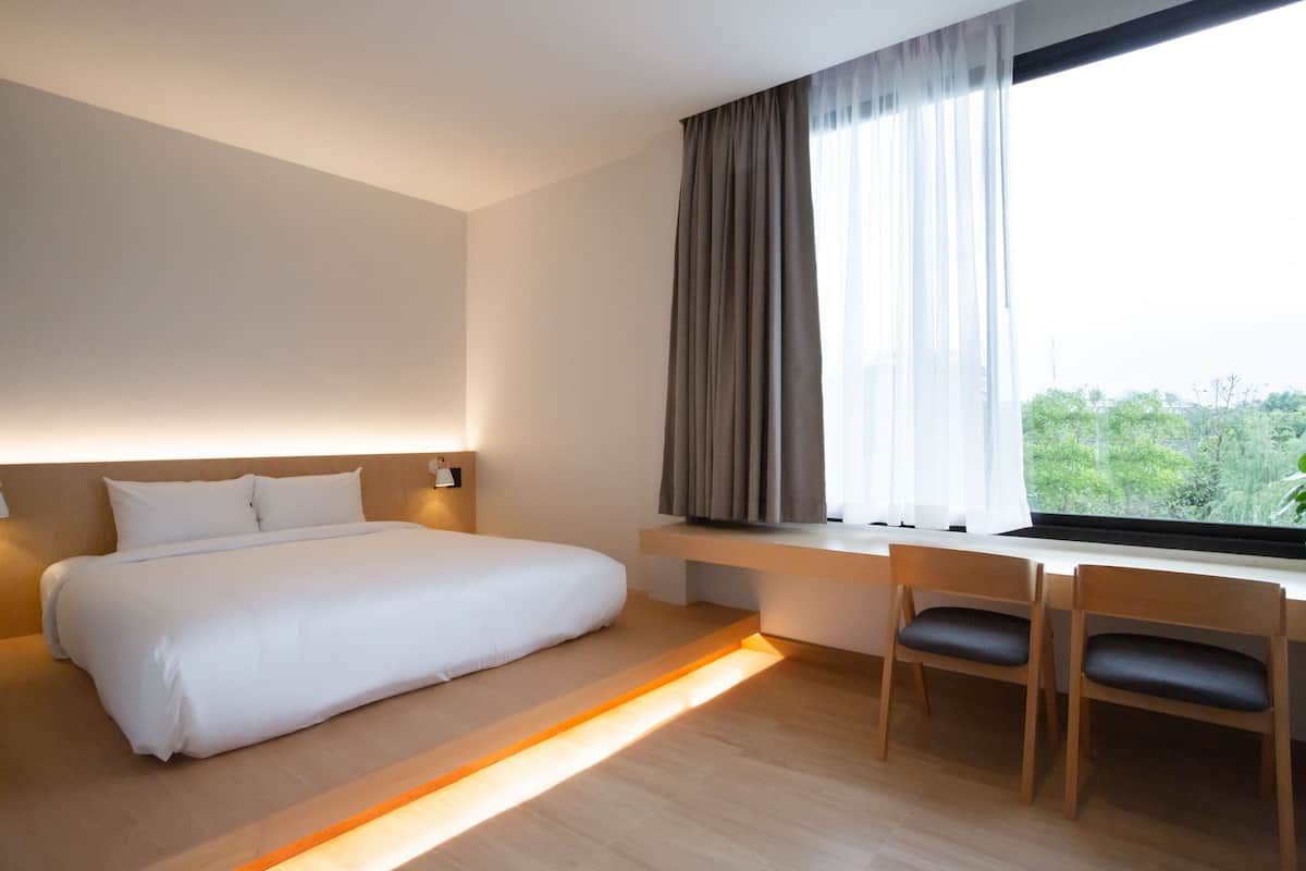 A modern hotel room with a large bed, a desk, and a window with curtains.