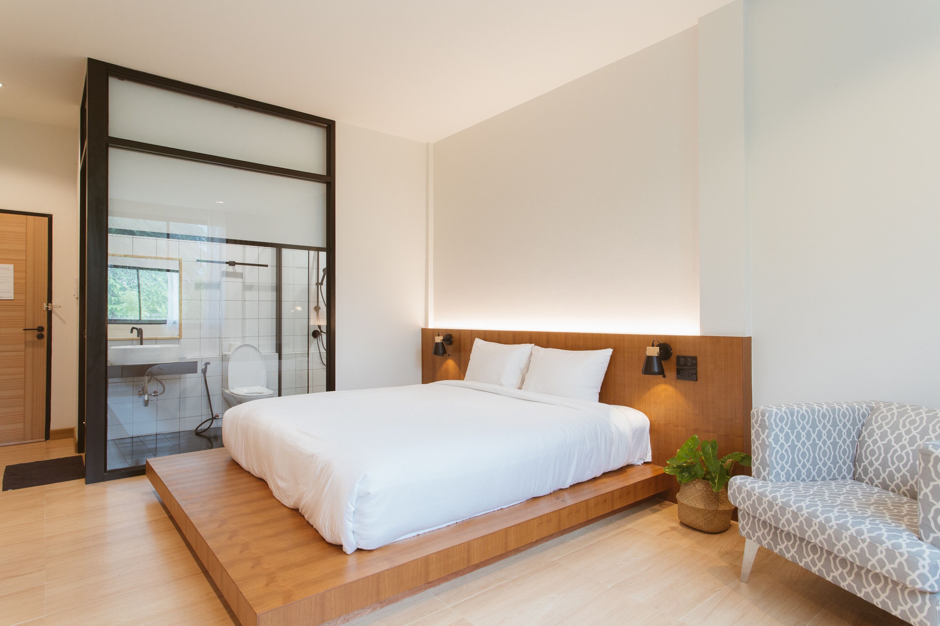 Un dormitorio moderno con una cama grande, una plataforma de madera, un sofá y una planta en maceta.
