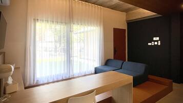 A room with a wooden desk, a white chair, a blue sofa, and a window with sheer curtains.