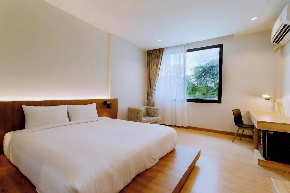 A hotel room with a large bed, a desk, a chair, and a window with curtains.