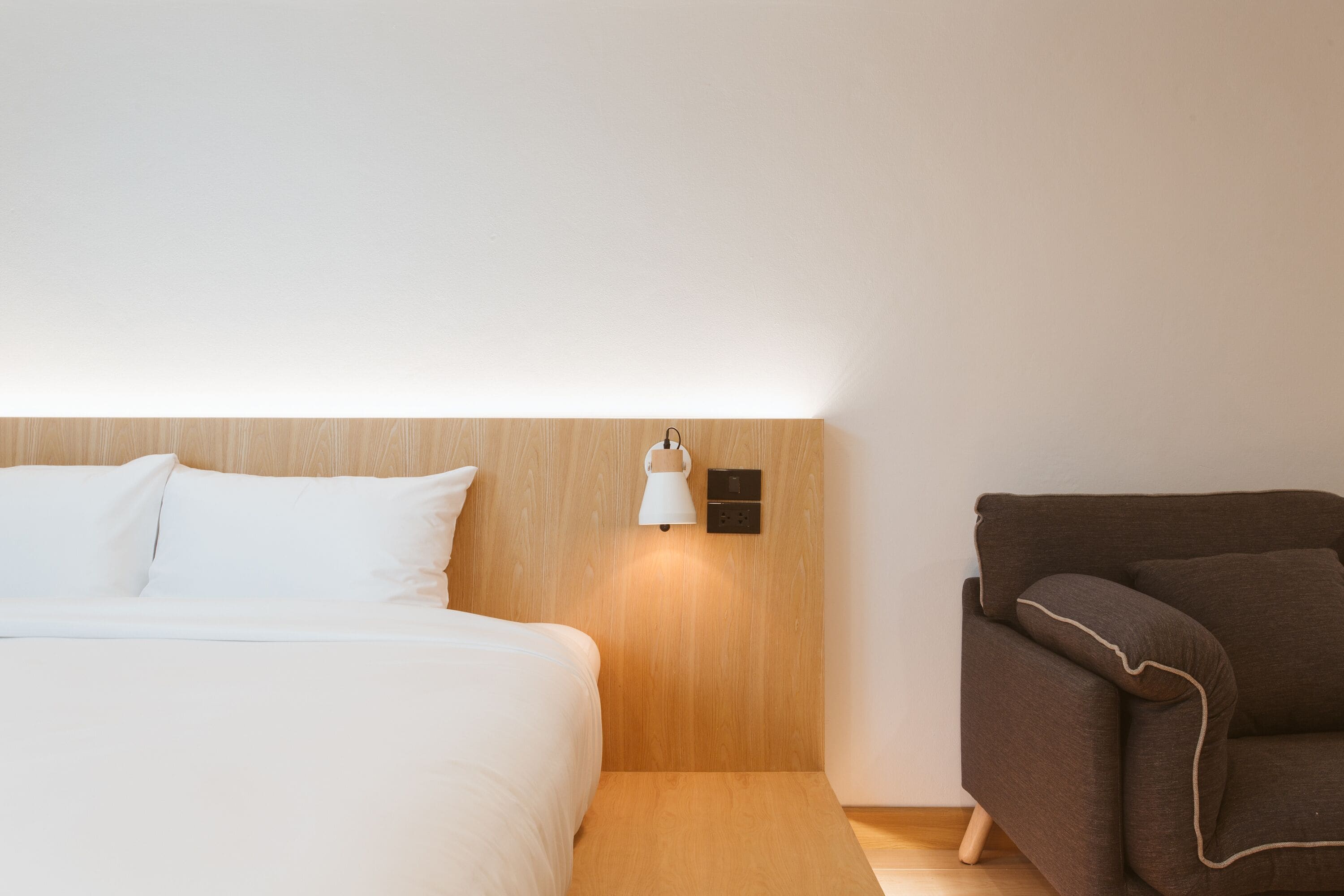 Quarto de hotel com uma cama, uma luminária na parede e um sofá.