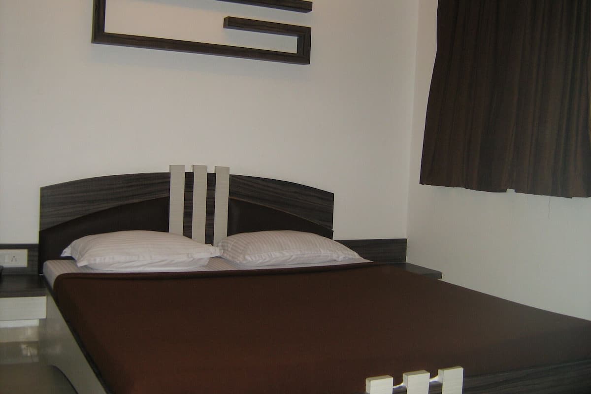 A neatly made bed with a dark headboard and two pillows, a bedside table with a lamp, and a wall-mounted light fixture.