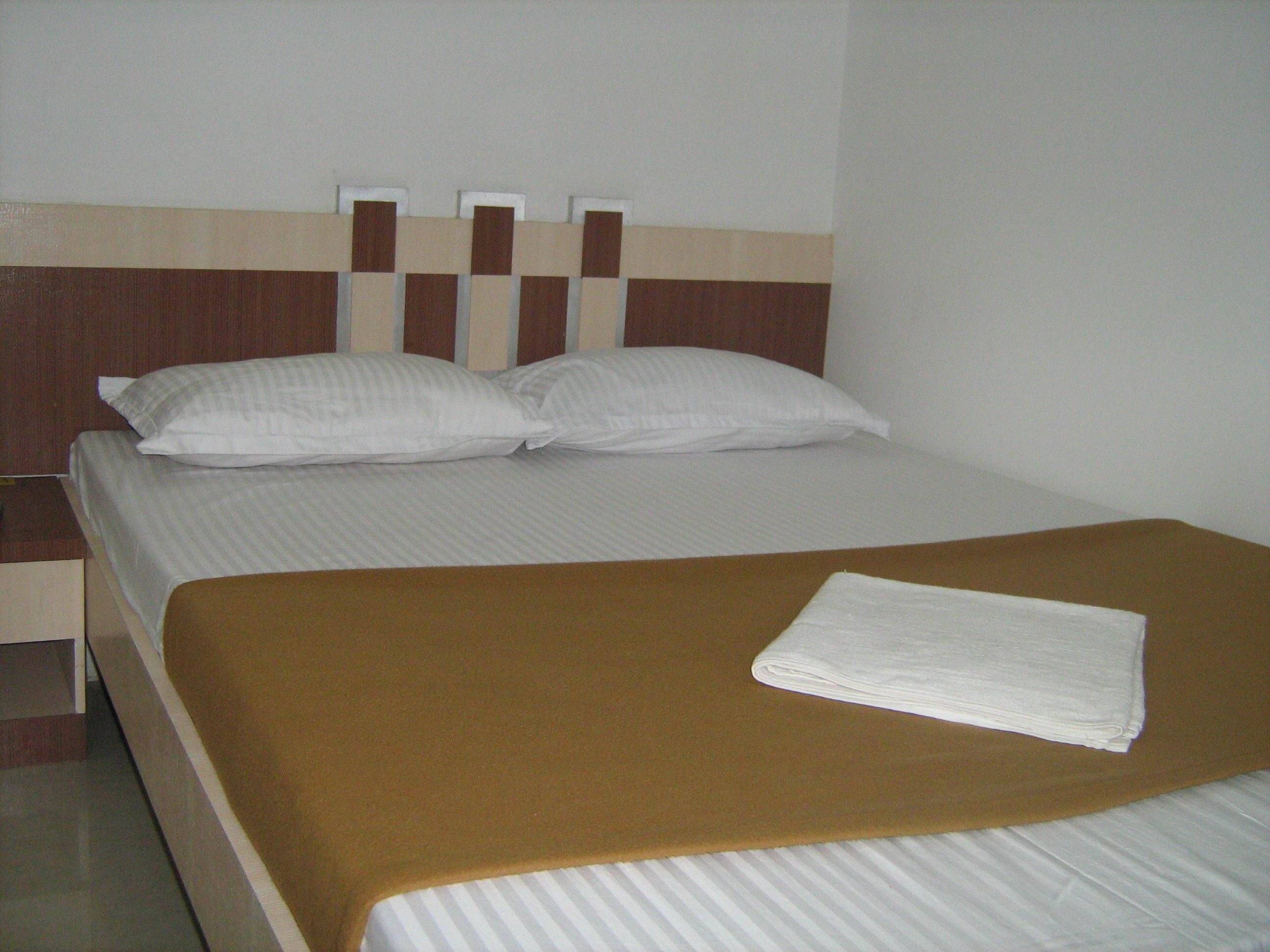A neatly made bed with a brown blanket and two pillows, a wooden headboard, and a white wall.