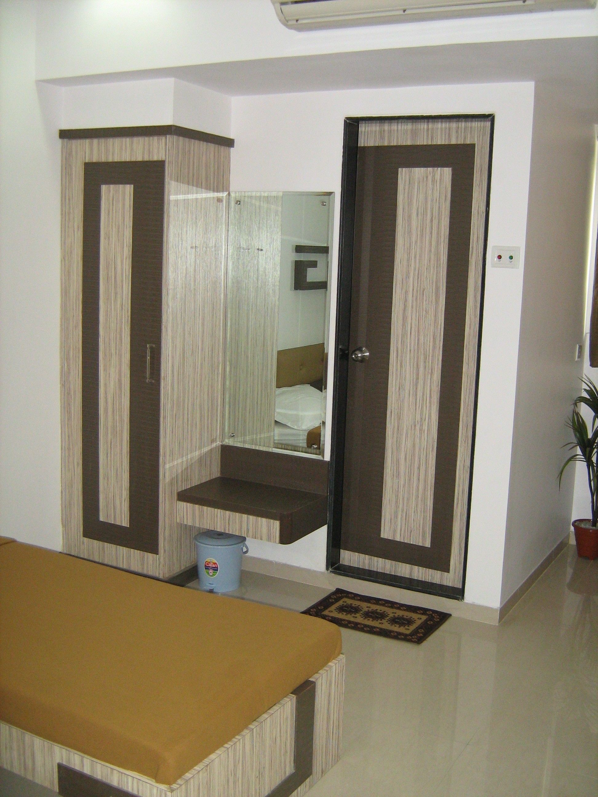 A room with a bed, a wardrobe, a small table, and a potted plant.