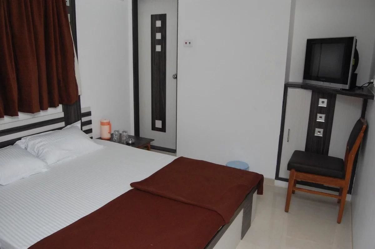 A hotel room with a bed, a desk, a chair, a television, and a wardrobe.