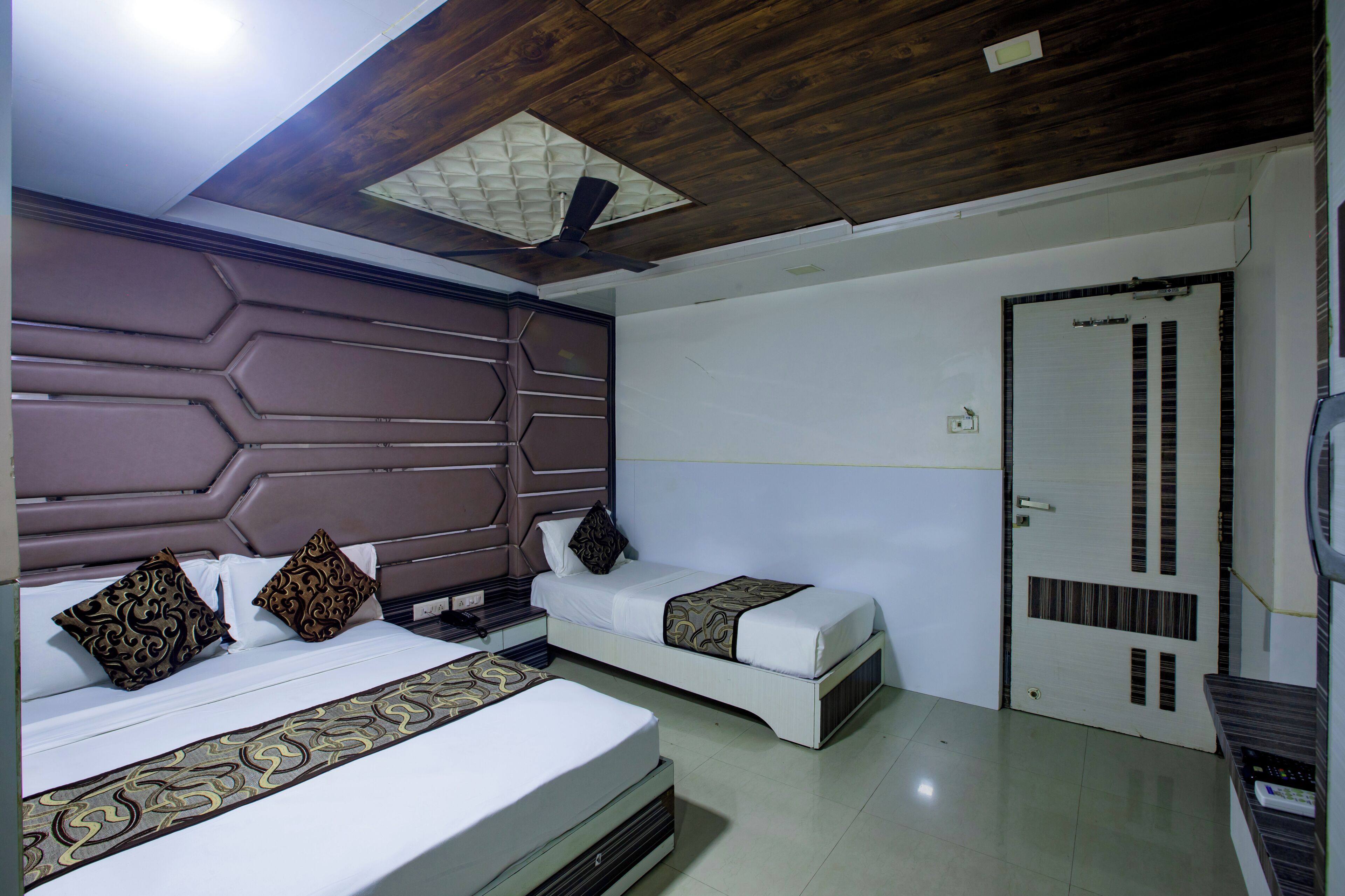 Una habitación de hotel con una cama grande, una cama más pequeña, un ventilador de techo y una puerta con un respiradero.