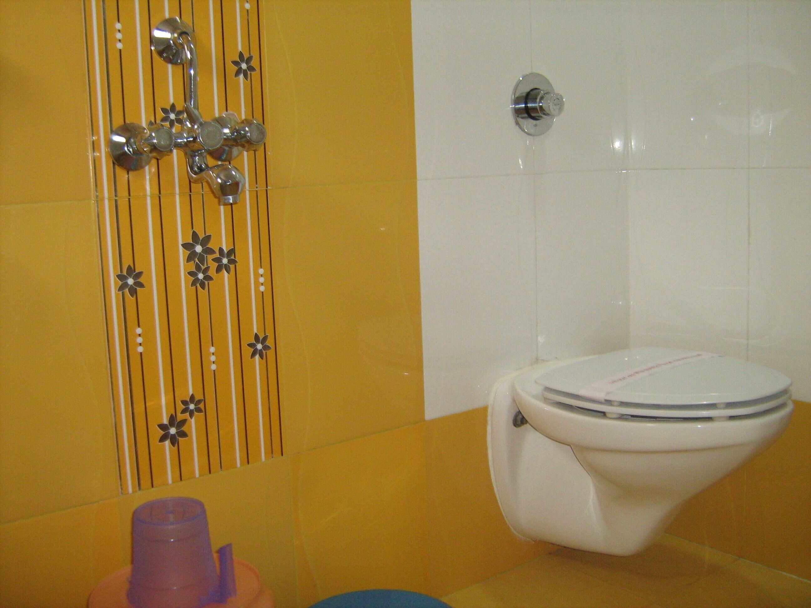 Un bany amb vàter, dutxa amb un disseny floral i un lavabo amb una tassa rosa.