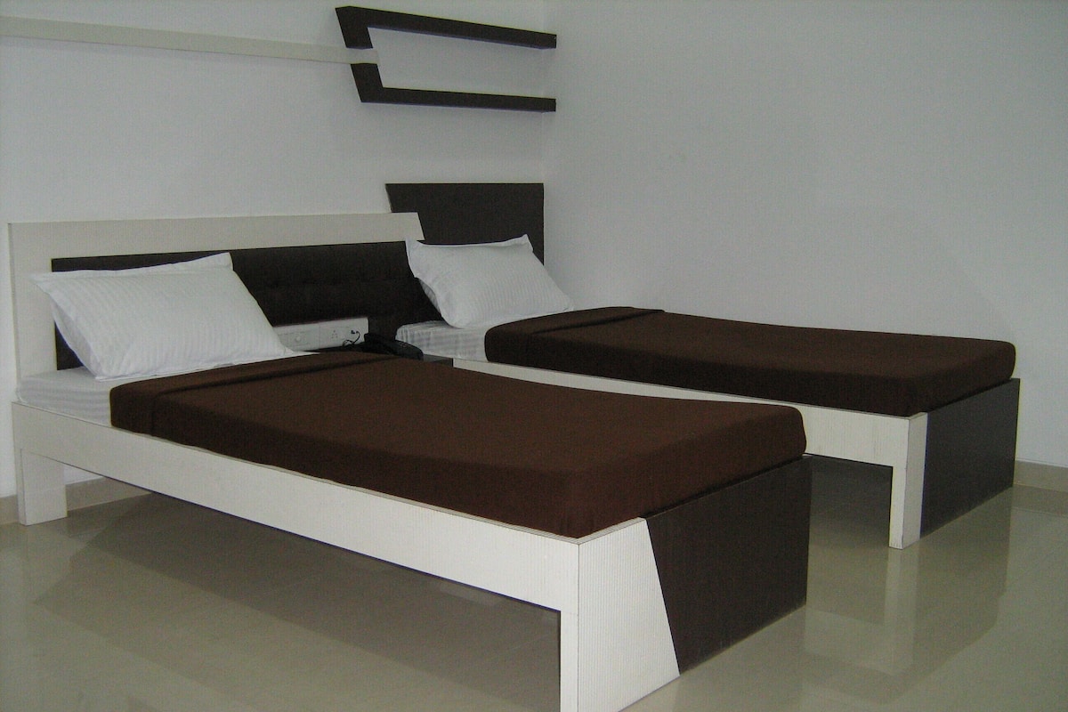 A modern bedroom with a white bed and bench, a dark headboard, and a white wall.