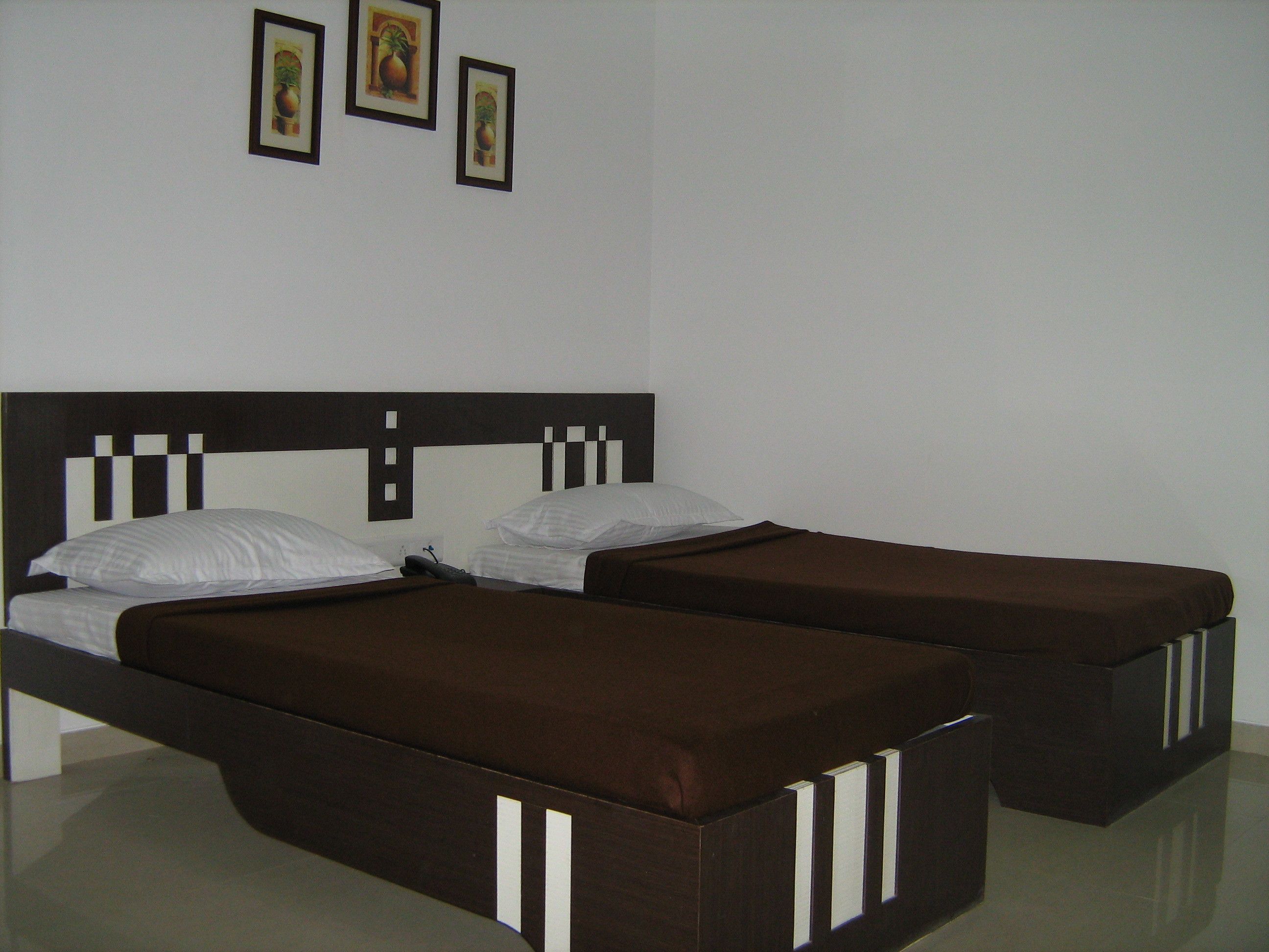 A hotel room with two single beds, a wooden headboard, and three framed pictures on the wall.