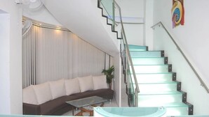 Una sala de estar moderna con un sofá curvo, una mesa de centro de vidrio y una escalera con barandilla de cristal.