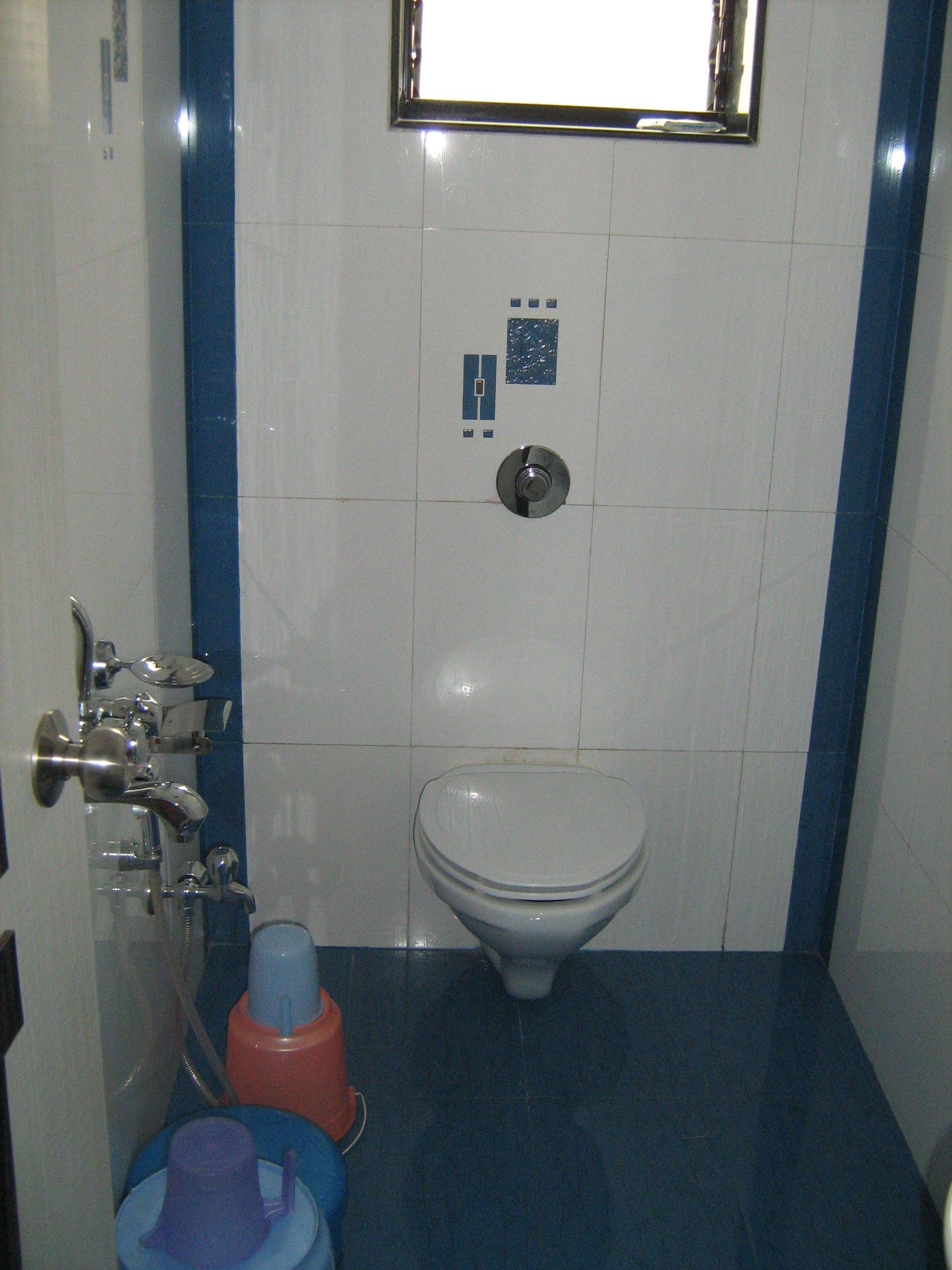 Un baño pequeño con inodoro, lavamanos y espejo. Las paredes están cubiertas de azulejos azules y blancos.