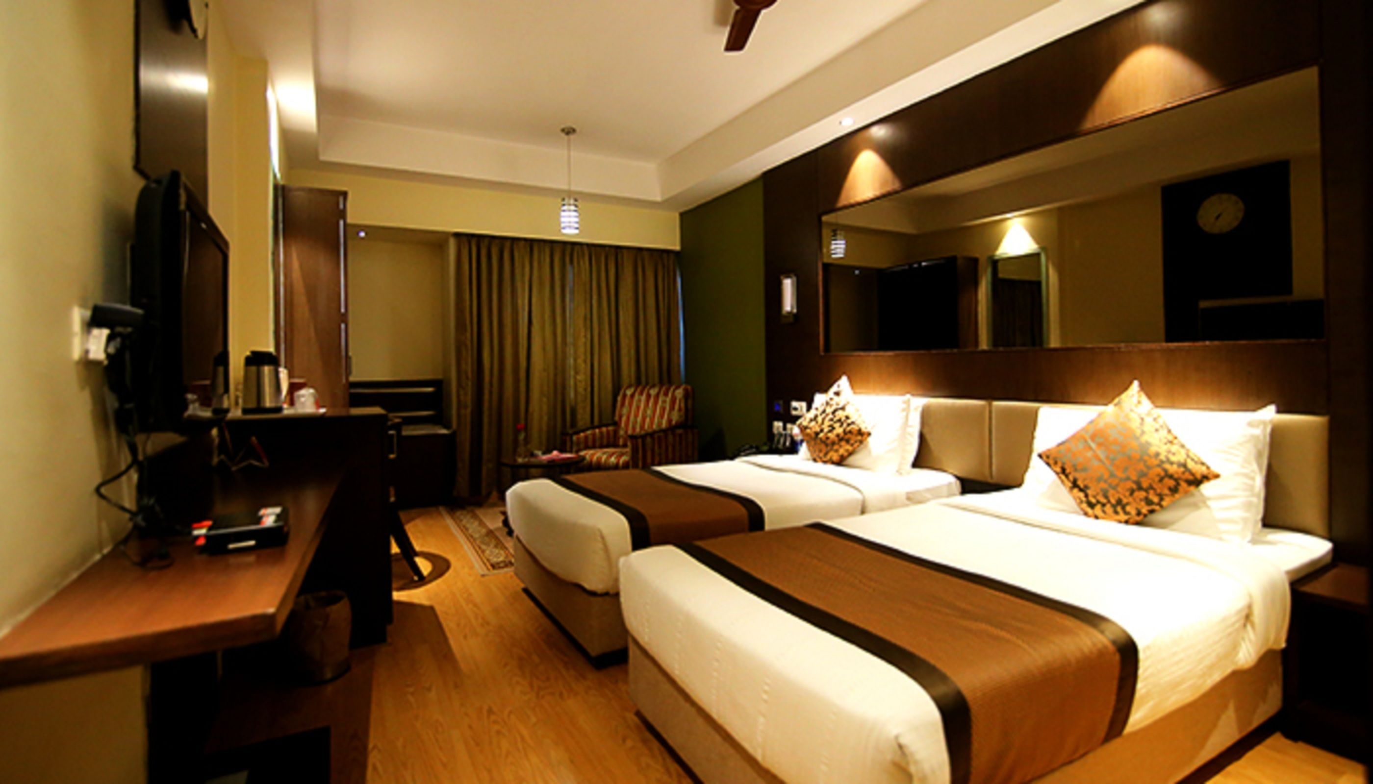 A hotel room with two beds, a desk, a chair, a television, and a mirror.