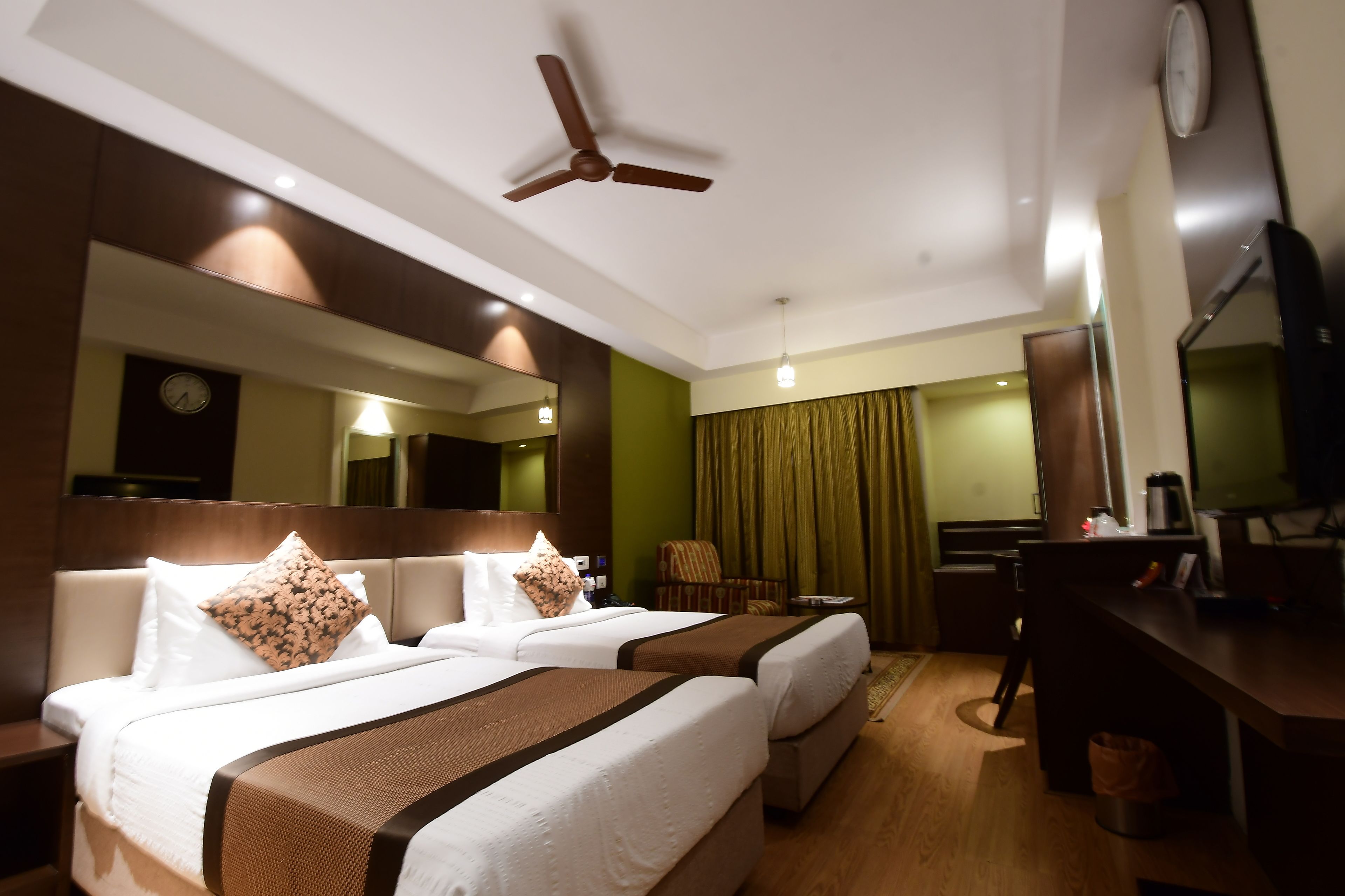Ein Hotelzimmer mit zwei Betten, einem Schreibtisch, einem Sessel, einem Fernseher und einem Deckenventilator.