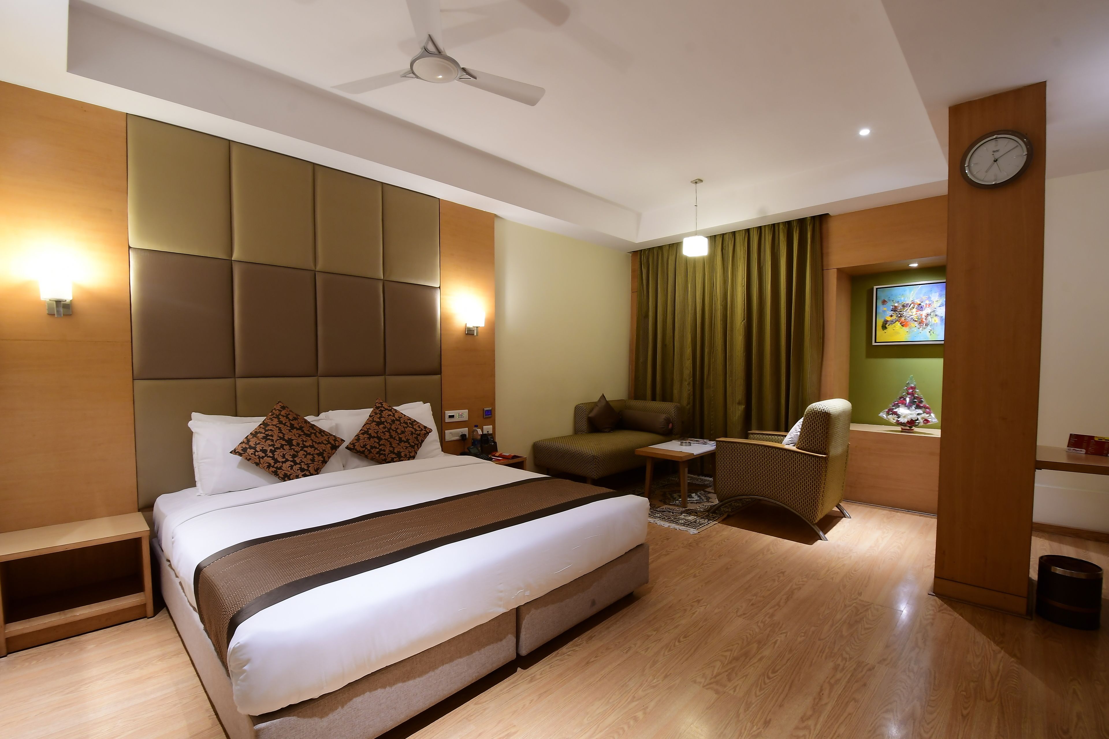 A hotel room with a large bed, a desk, a chair, a clock, and a small Christmas tree.
