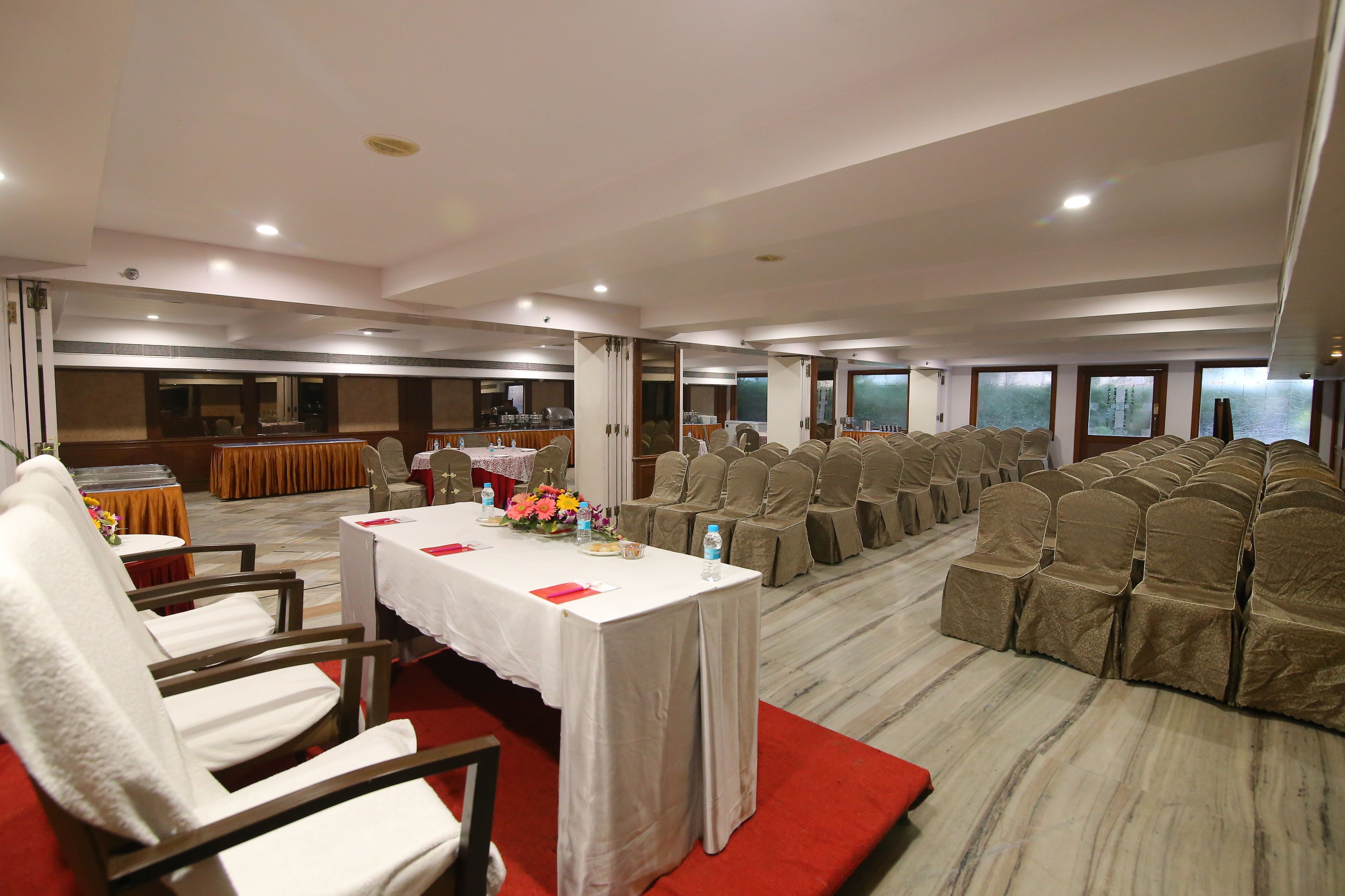 Un salón de conferencias con filas de sillas, una mesa con mantel blanco y alfombra roja.