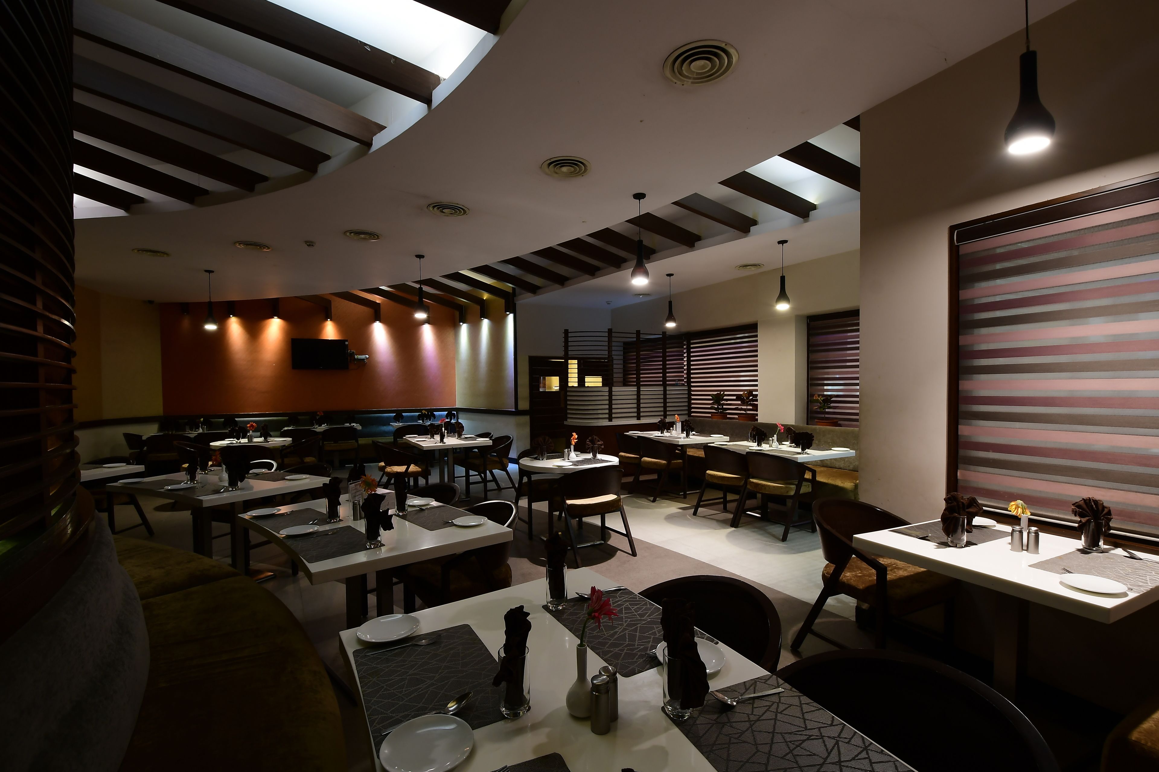 Un restaurante moderno con techo curvo, varias mesas de comedor e iluminación colgante.