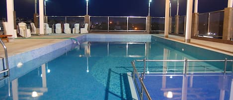 Area piscina con vasca azzurra e cristallina, lettini e zona relax coperta di sera.